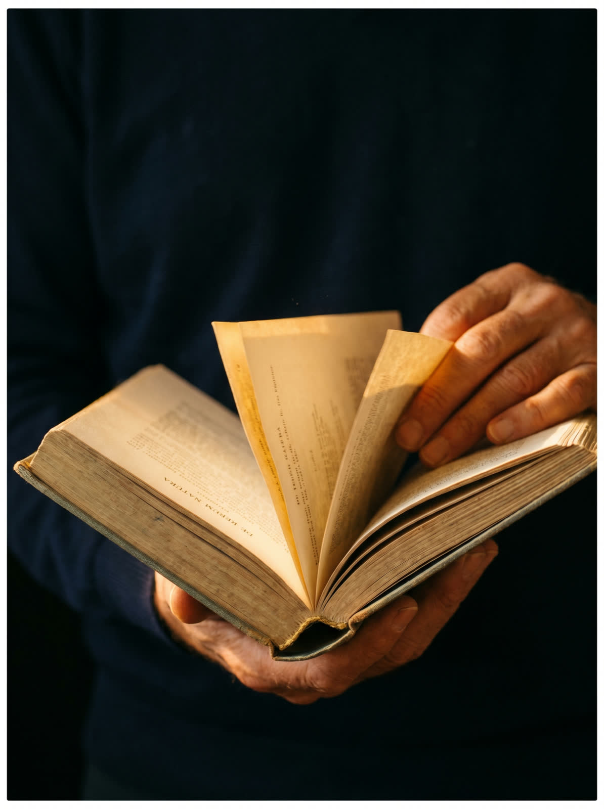 Mãos folheando um livro antigo sob luz quente
